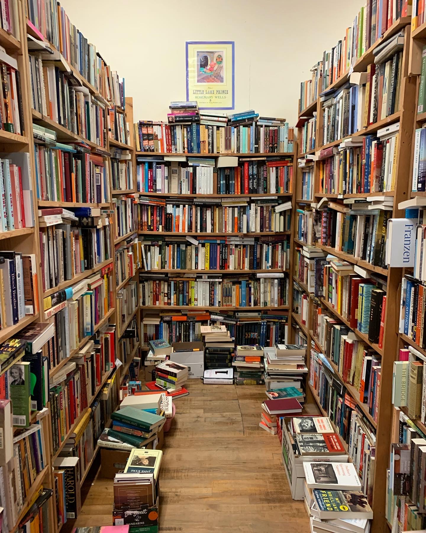 A small corridor in a bookstore that is crammed floor to ceiling with books and book stacks on the floor. 