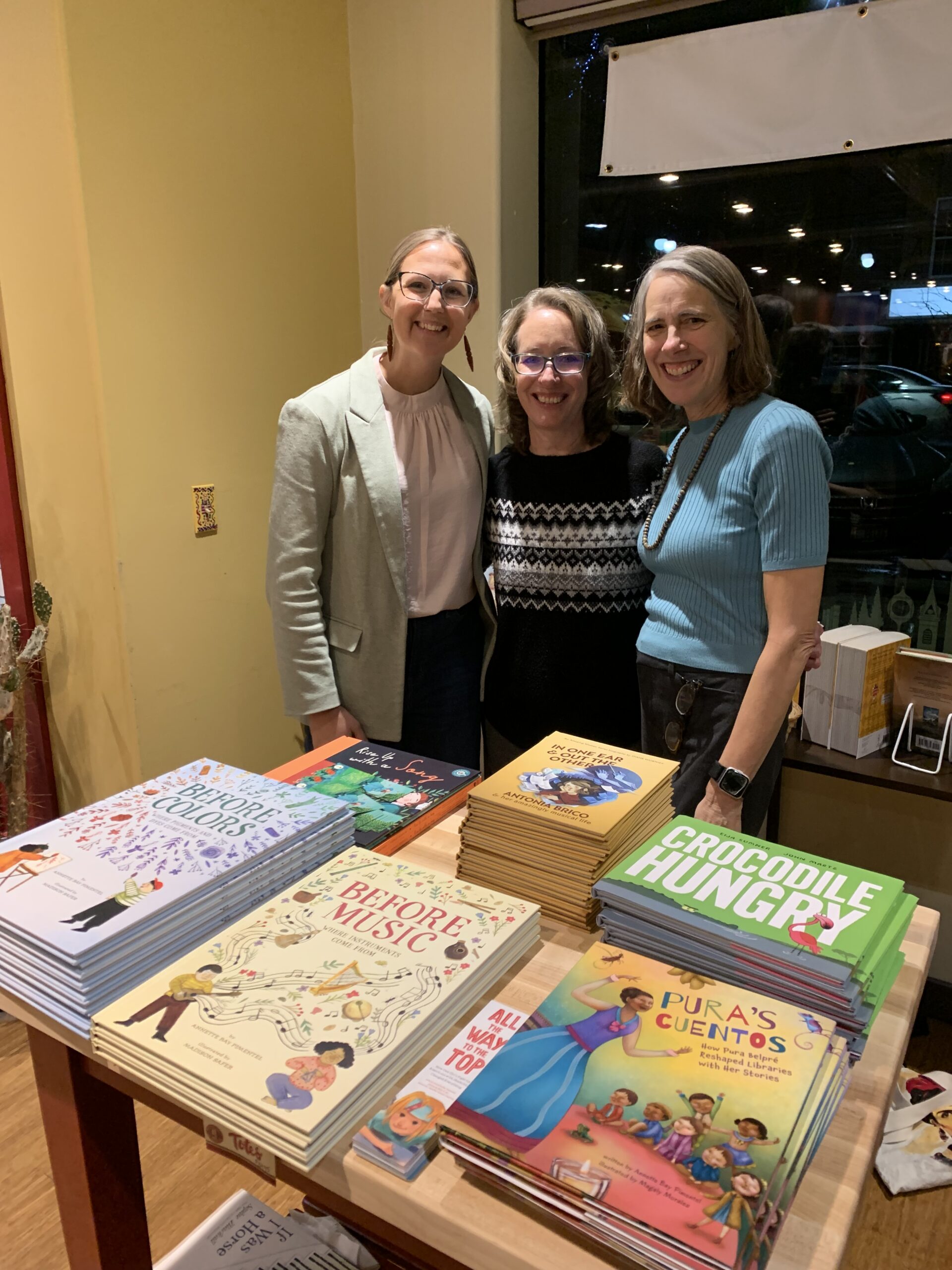 Three book friends smiling in front of a table of picture books in BookPeople of Moscow.