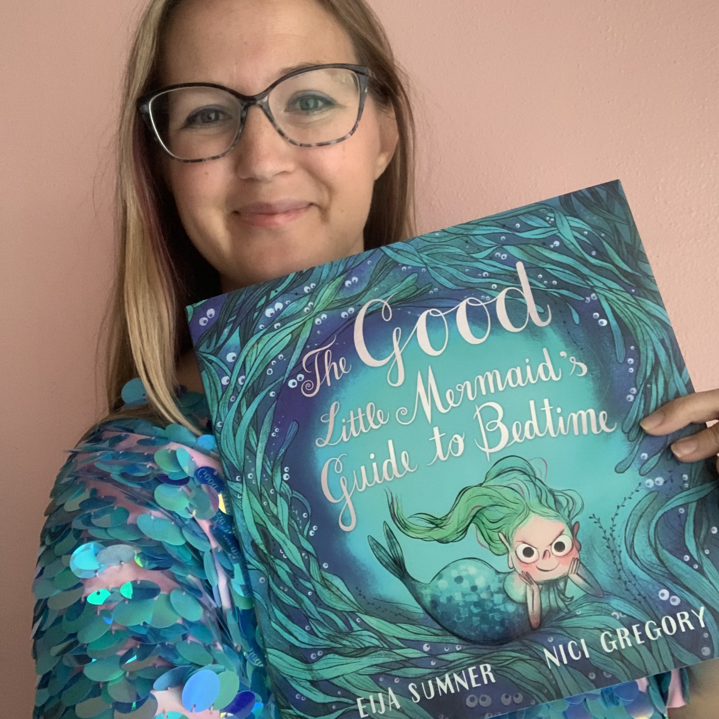 Children's author Eija Sumner wearing glasses and a blue sparkly shirt and holding her book with a blue ocean cover.