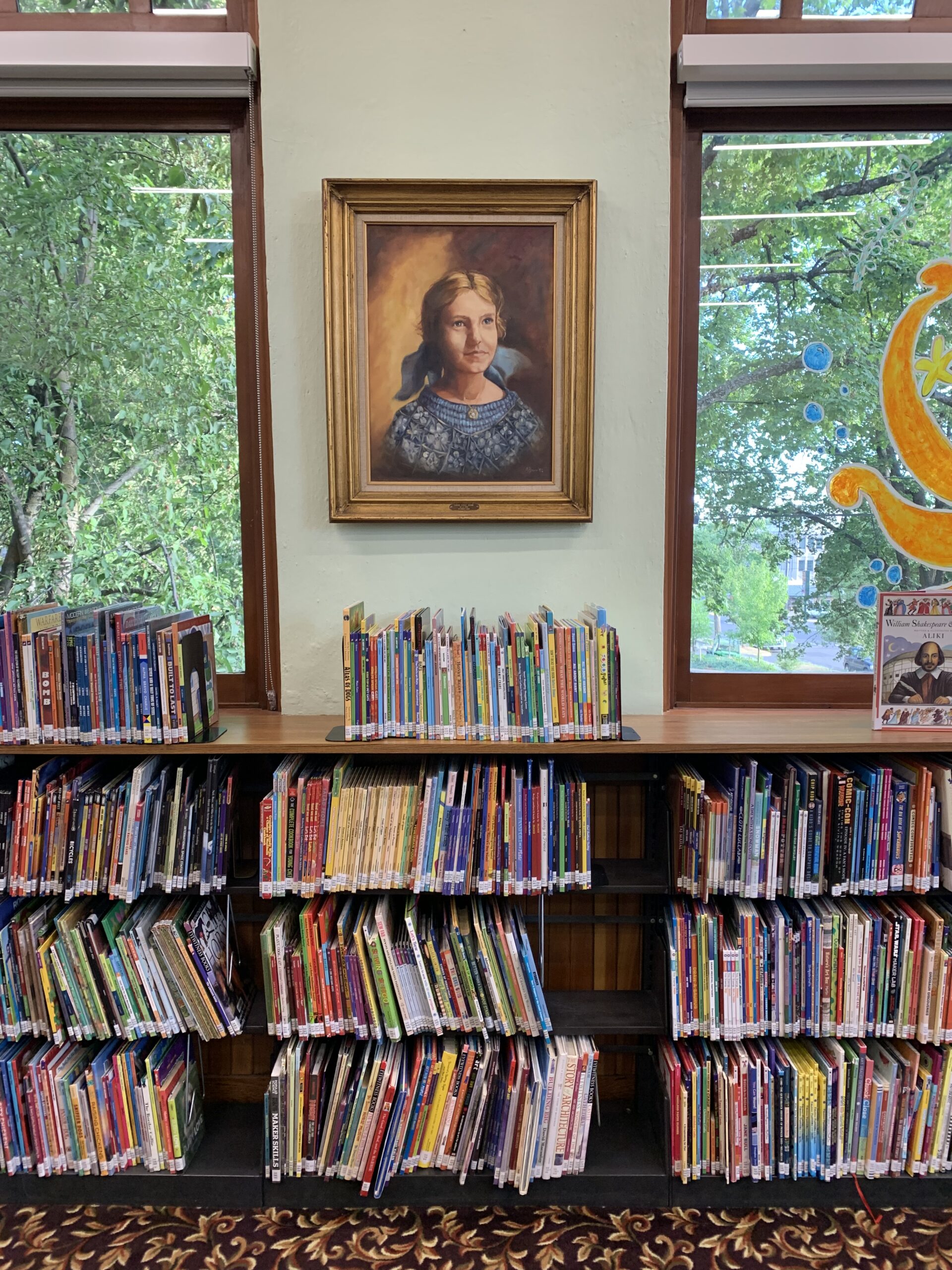 Carol Ryrie Brink portrait centered between two windows and library shelves in the Latah Library