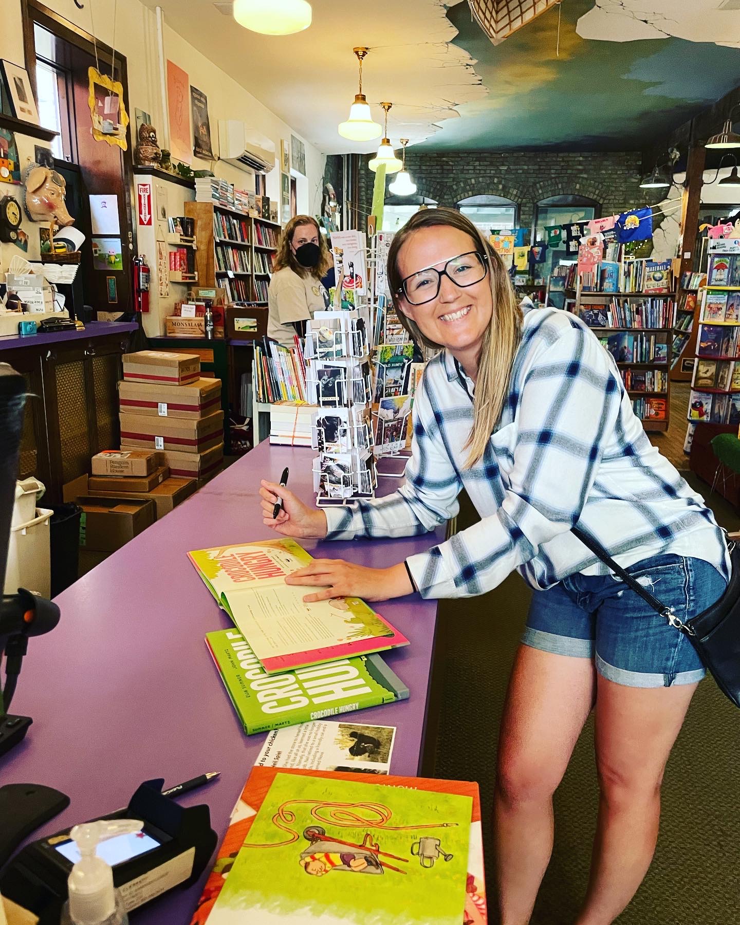 Eija Sumner wearing large glasses and signing copies of her books in the Wild Rumpus bookshop