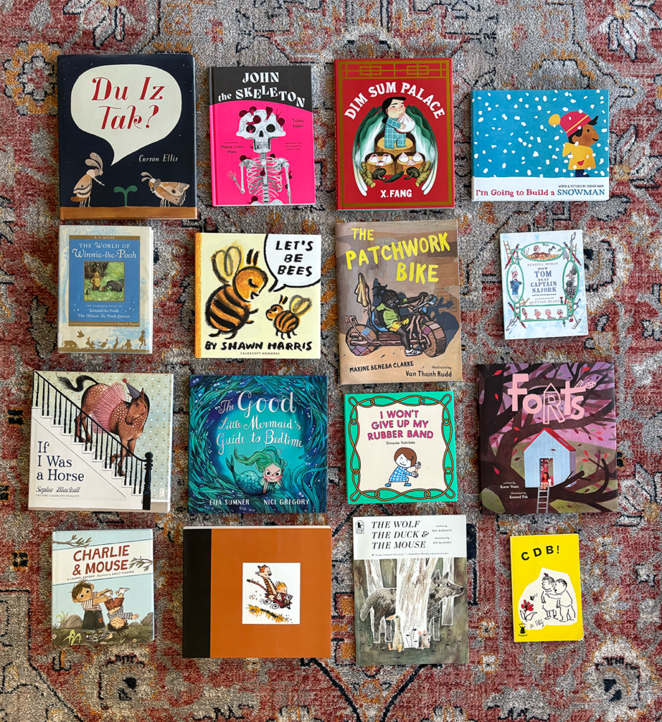 A collection of mostly picture books on a rug.
